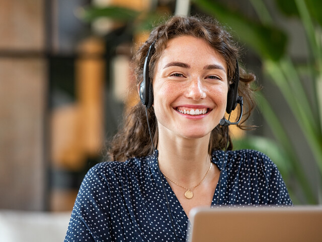 Portrait einer lächelnden jungen Frau, welche Businesskleidung und ein Headset trägt.