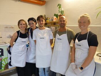 Fünf Personen mit weißen Caritas-Küchenschürzen stehen zu einem Gruppenfoto zusammen.