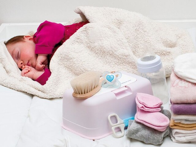 Ein Baby liegt in eine Decke eingewickelt neben vielen Produkten für Babies.