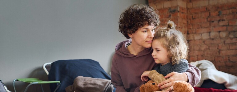 Eine Mutter hält ihre Tochter, die einen Teddybär festhält, schützend im Arm.