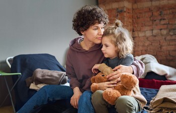 Eine Mutter hält ihre Tochter, die einen Teddybär festhält, schützend im Arm.