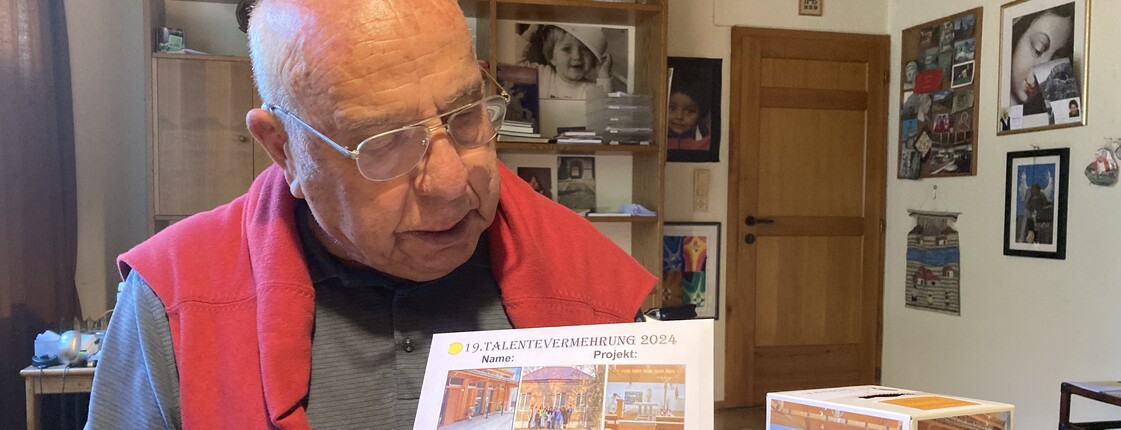 Ein Senior mit Brille zeigt ein Plakat und eine Spendenbox her.