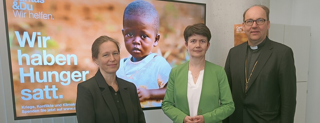 Drei Personen stehen vor einem Bildschirm mit Kampagnensujet zu einem Pressefoto zusammen.
