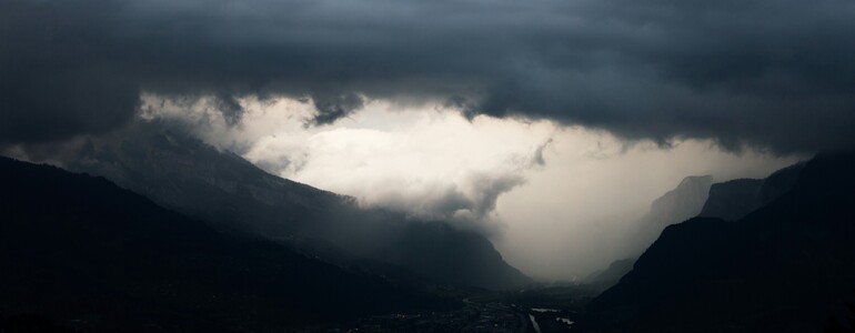 Über einem Tal in den Alpen zieht ein bedrohliches Unwetter mit schwarzen Wolken und Starkregen auf.