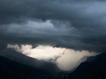 Über einem Tal in den Alpen zieht ein bedrohliches Unwetter mit schwarzen Wolken und Starkregen auf.