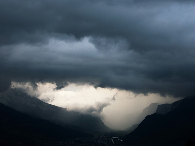 Über einem Tal in den Alpen zieht ein bedrohliches Unwetter mit schwarzen Wolken und Starkregen auf.
