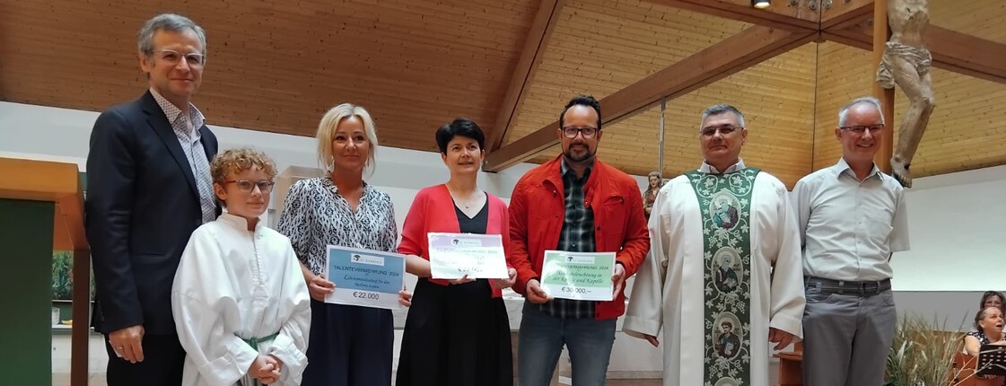 Sieben Personen stehen in einer Kirche und drei Personen in der Mitte präsentieren Spendenschecks.