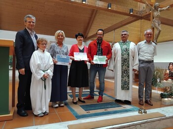 Sieben Personen stehen in einer Kirche und drei Personen in der Mitte präsentieren Spendenschecks.