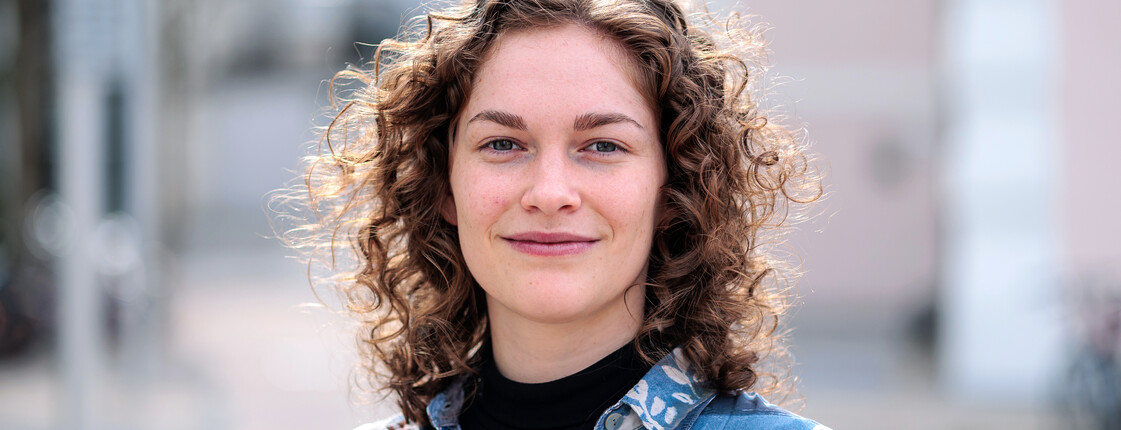 Freiwilliges Soziales Jahr Portrait einer jungen Frau, die ein buntes Hemd trägt, vor einem Gebäude.