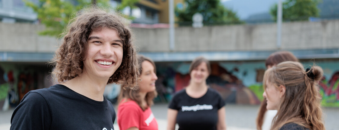 Portrait eines Freiwilligen mit schwarzem youngCaritas T-Shirt, der mit vier Kolleginnen auf einem großen Platz steht.