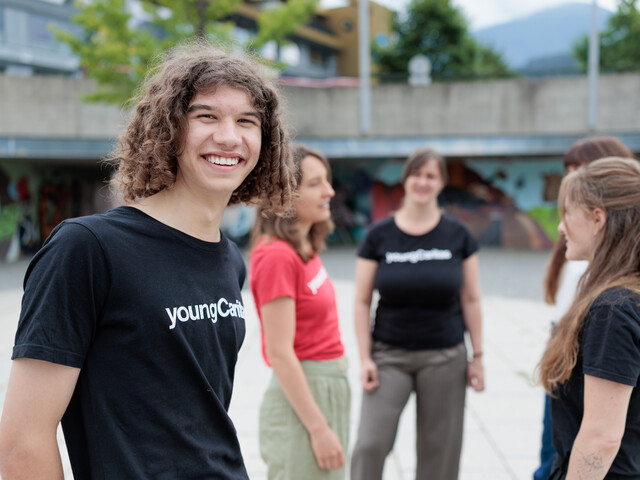 Portrait eines Freiwilligen mit schwarzem youngCaritas T-Shirt, der mit vier Kolleginnen auf einem großen Platz steht.