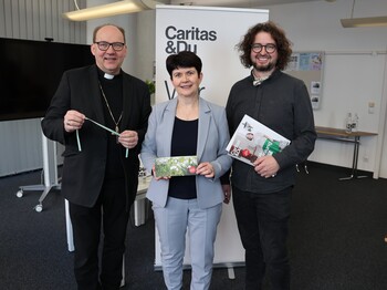 Ein Mann, eine Frau und noch ein Mann stehen nebeneinander und lachen in die Kamera. In den Händen halten sie Broschüren.