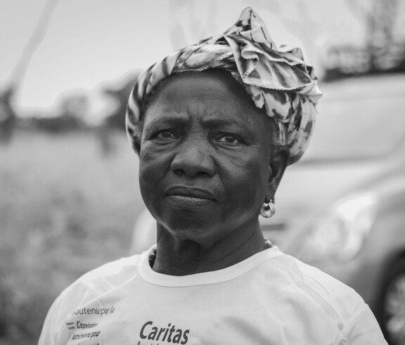 Eine Frau blickt in die Kamera; sie steht draußen und trägt ein Kopftuch sowie ein T-Shirt mit Projektaufdruck.