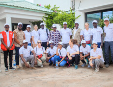 Eine Gruppe von Menschen steht und sitzt gemeinsam für ein Gruppenfoto vor einem Gebäude.