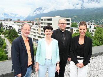 Vier Personen stehen auf einem Dach zu einem Gruppenfoto zusammen. Im Hintergrund ein großer Rohbau.