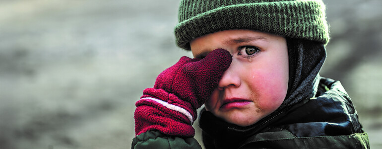 Ein weinendes Kind mit Mütze und roten Handschuhen wischt sich eine Träne aus dem Augenwinkel.