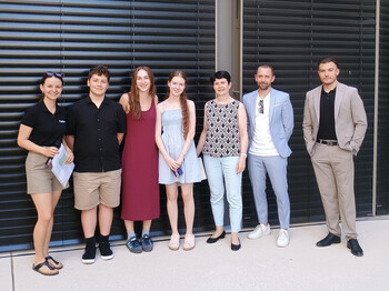 Sieben Personen stehen nebeneinander vor den schwarzen Schalusien einer Hausfassade zu einem Gruppenfoto zusammen.