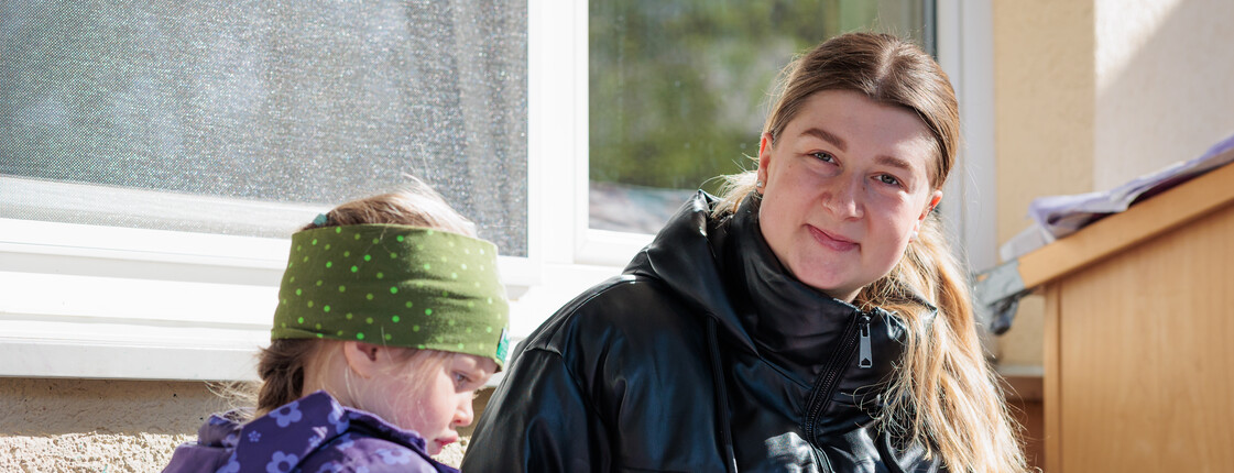 Eine junge Frau und ein Kindergartenkind sitzen mit Winterkleidung im Freien und malen mit Wasserfarben.