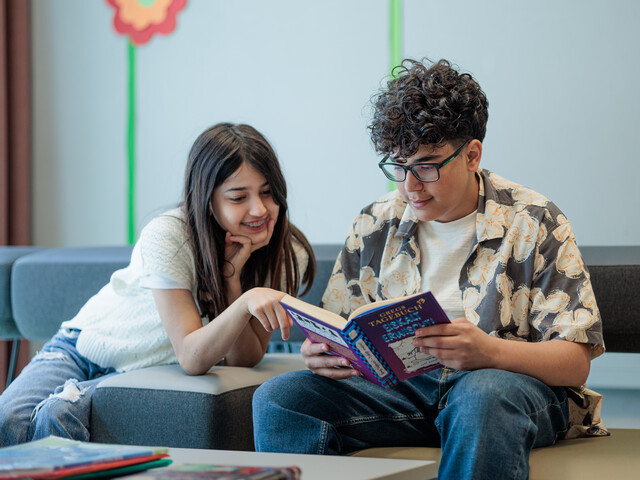 Ein Junge und ein Mädchen sitzen auf einem Sofa und lesen in einem Buch.