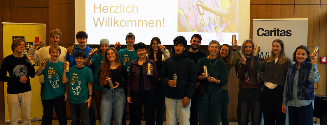 Eine große Gruppe an Jugendlichen stehen um Caritas Direktorin Elisabeth Rathgeb und halten Spraydosen.