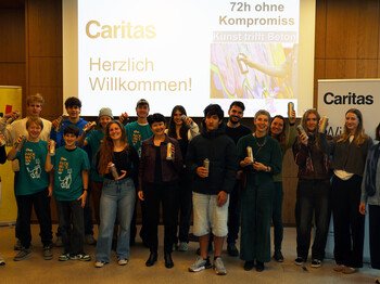Eine große Gruppe an Jugendlichen stehen um Caritas Direktorin Elisabeth Rathgeb und halten Spraydosen.