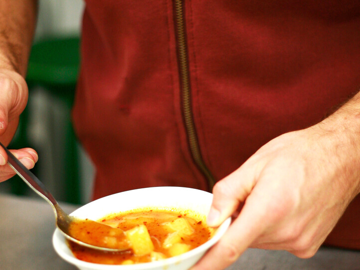 Ein Mann, der einen roten Hoodie trägt, löffelt in einer Schüssel mit Kartoffelsuppe.