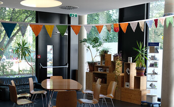 Ein offener, möblierter Raum mit großer Fensterfassade und einem Tisch mit Stühlen.