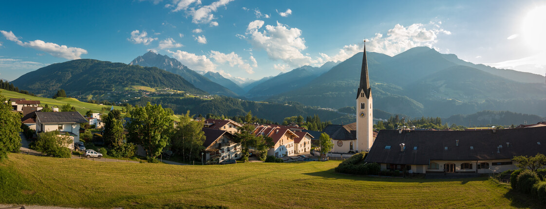 Panorama einer kleinen Gemeinde mit Kirchturm vor Tiroler Bergkulisse.