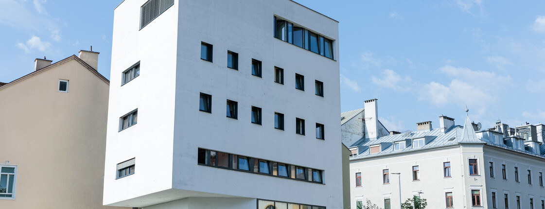 Ein weißer Neubau steht in einem Bahnhofsviertel zwischen alten Gebäuden.