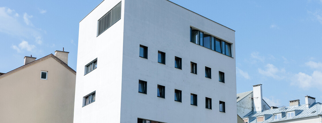 Ein weißer Neubau steht in einem Bahnhofsviertel zwischen alten Gebäuden.