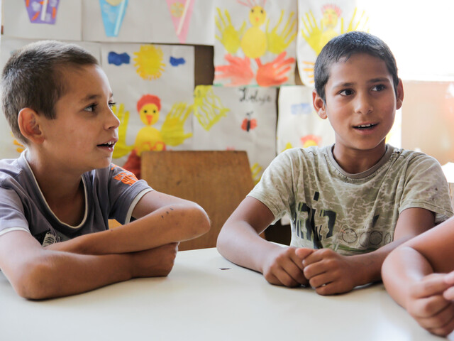 Drei Jungen sitzen in einem Kindergarten an einem Tisch und reden miteinander.