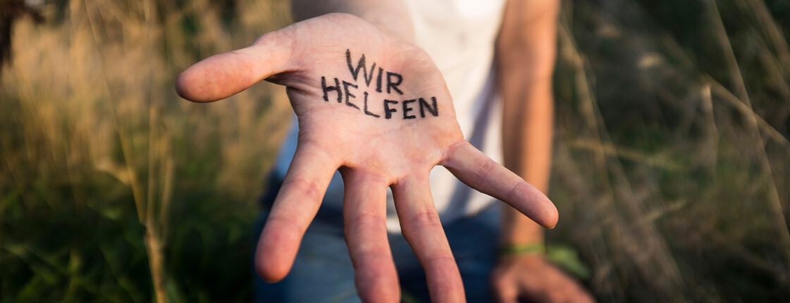 Nahaufnahme einer ausgestreckten Hand auf der "Wir helfen" geschrieben steht.