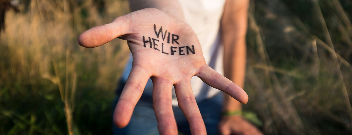 Über uns Nahaufnahme einer ausgestreckten Hand auf der "Wir helfen" geschrieben steht.