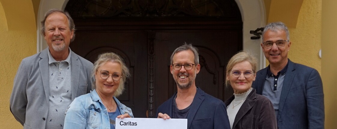 Benefizmesse aller Chöre in Landeck Fünf Personen stehen zu einem Gruppenfoto zusammen und halten einen Spendenscheck.