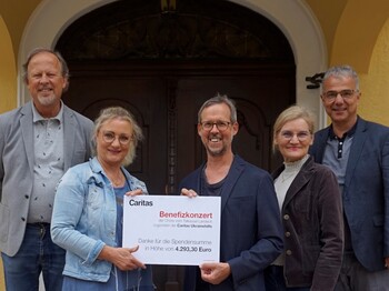 Fünf Personen stehen zu einem Gruppenfoto zusammen und halten einen Spendenscheck.