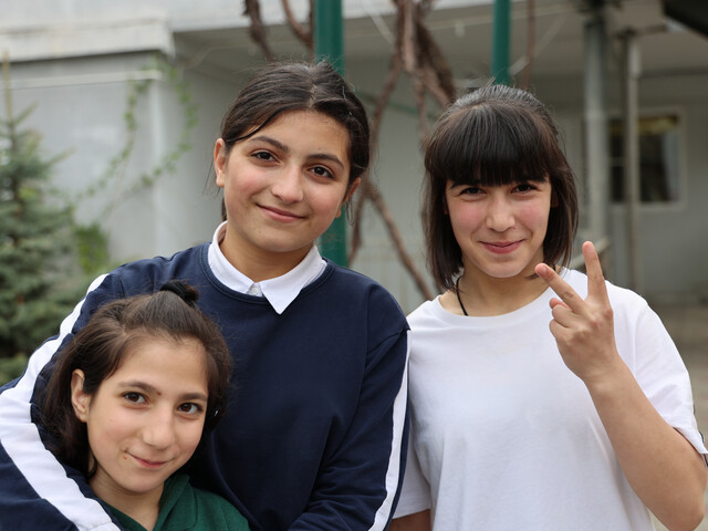 Drei lächelnde Schüler*innen stehen zu einem Gruppenfoto zusammen.