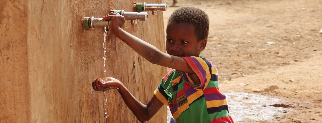 Ein Junge in Burkina Faso lässt Wasser aus dem Hahn eines Trinkwasserbrunnen laufen.