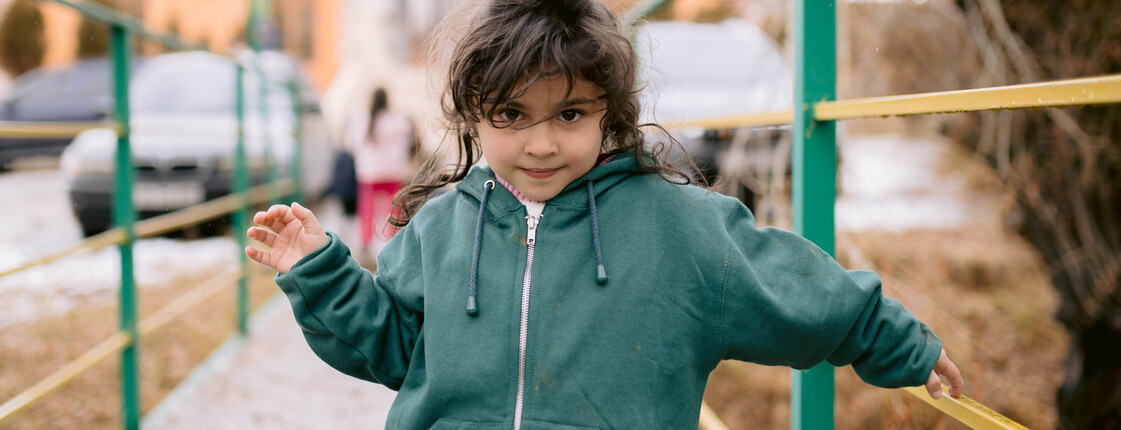 Portrait eines Mädchens in einem grünen Hoodie vor einem Haus mit Parkplatz.