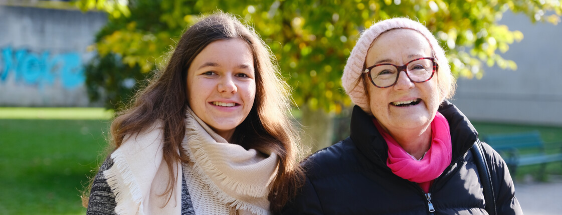 Zwei Frauen stehen Arm in Arm in einem Park.