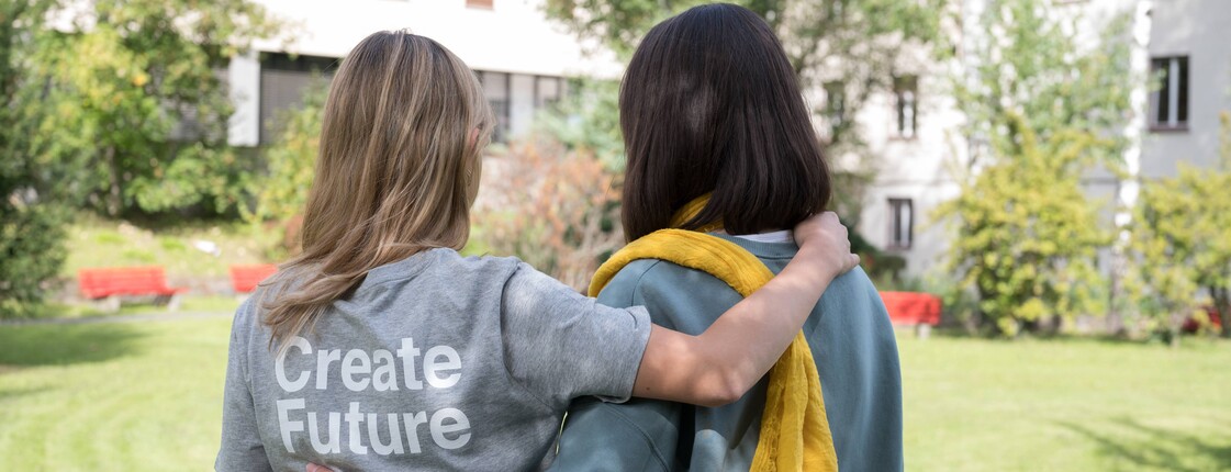 Zwei Frauen stehen mit dem Rücken zur Kamera in einem Garten.
