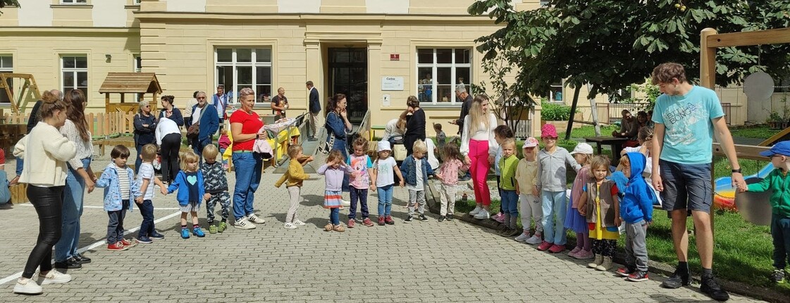 Viele Kinder stehen vor einer Kinderbetreuungseinrichtung in der Reihe und halten Hände.