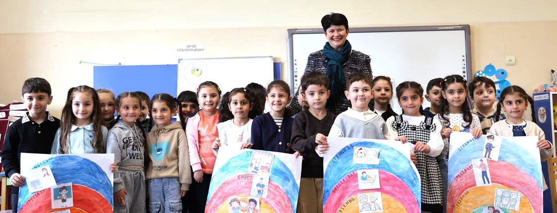 Eine Frau steht in einem Klassenzimmer in Armenien hinter einer großen Gruppe an Schulkindern, die selbstgemalte Plakate präsentieren.