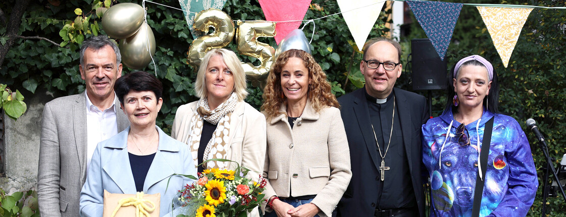 Sechs Perosnen stehen in einem Garten zu einem Gruppenfoto zusammen.