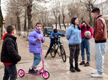 Sechs Kinder spielen auf den Gehweg neben einer Straße.