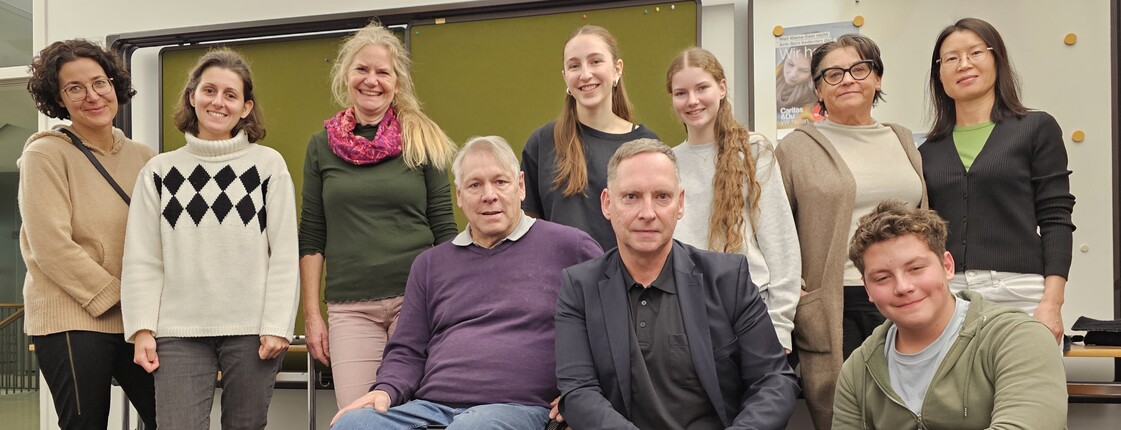 Zehn Personen, darunter Menschen mit Behinderung im Rollstuhl sitzend, rücken in einem Seminarraum zu einem Gruppenfoto zusammen.