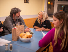 Mehrere Personen sitzen an einem Tisch zusammen. Eine Caritas Mitarbeiterin führt ein Gespräch mit einem Besucher der Einrichtung.