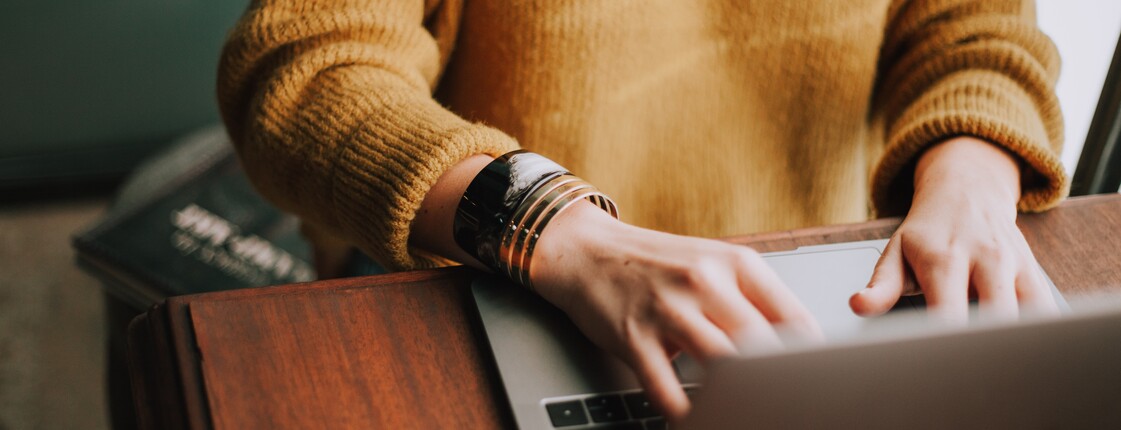 Caritas Online Beratung Eine junge Frau arbeitet am Laptop, ihre Hände auf der Tastatur sind im Fokus, ihr Gesicht nicht zu sehen.