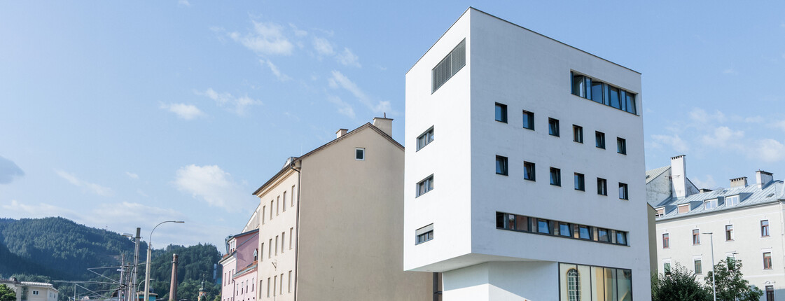 Ein weißer Neubau steht in einem Bahnhofsviertel zwischen alten Gebäuden.