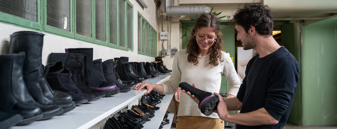 Second-Hand-Shopping und Beschäftigungsmöglichkeiten Ein Mann und eine Frau stehen in einem Second-Hand-Shop vor Regalen mit schwarzen Schuhen und sortieren gemeinsam Schuhe aus.