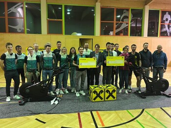 Gruppenfoto in einer Sporthalle. Zwei Perosnen präsentieren jeweils einen Spendenscheck über 11.500 Euro.